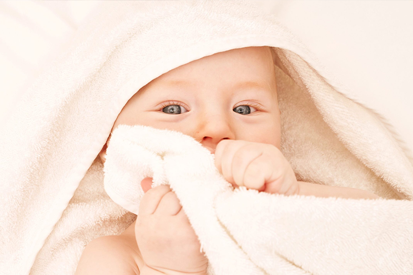 Cute baby with blue eyes wrapped in a cozy white towel.