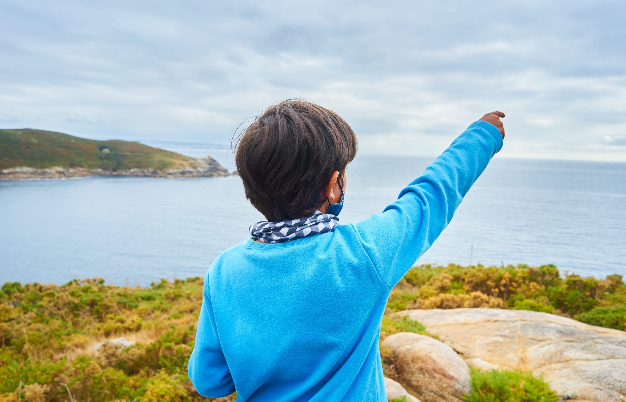 Child pointing towards the ocean with scenic landscape background.