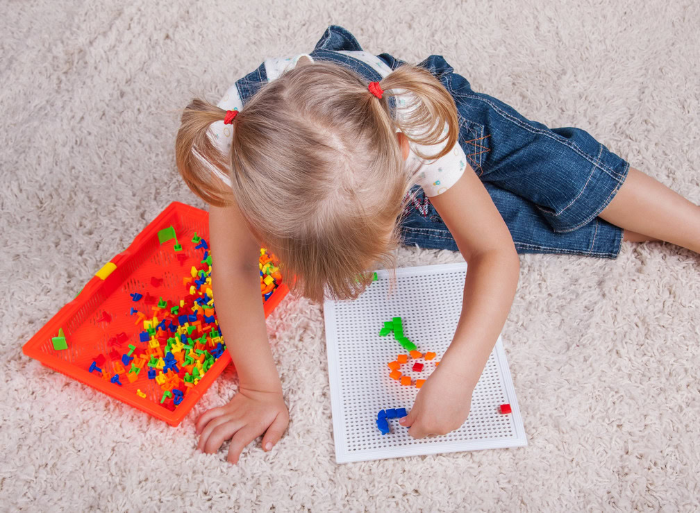 Young girl assembling colorful LEGO pieces on a white board.
