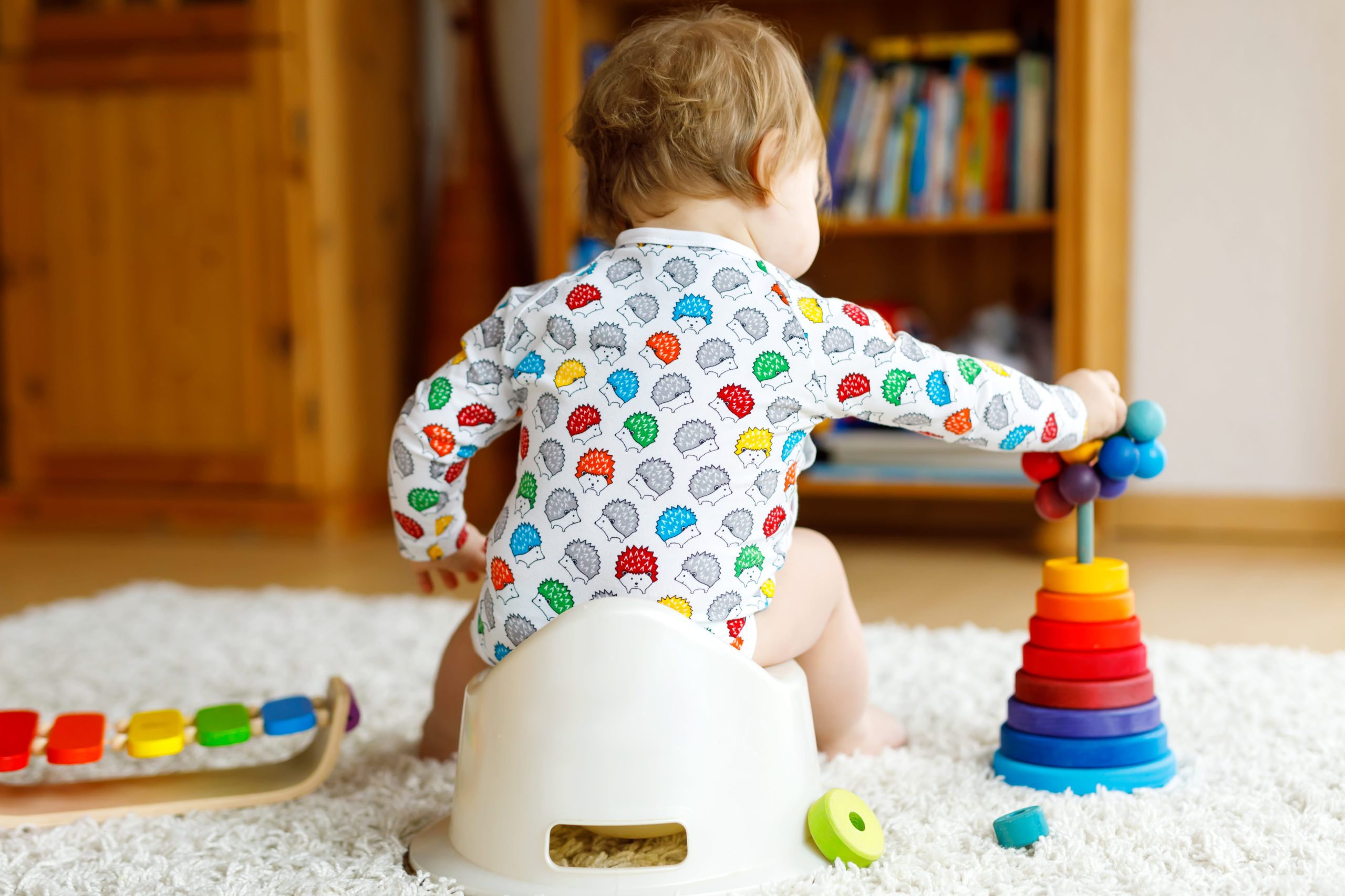 Baby stacking colorful rings toy on a white carpet in a cozy room.