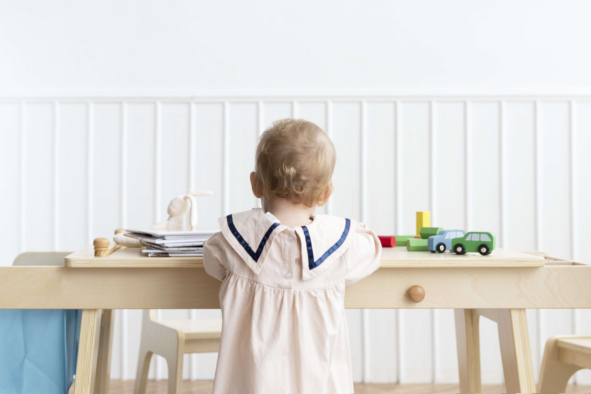 Child Playing with Toys at Desk Child with blonde hair playing with toy cars at a wooden desk.