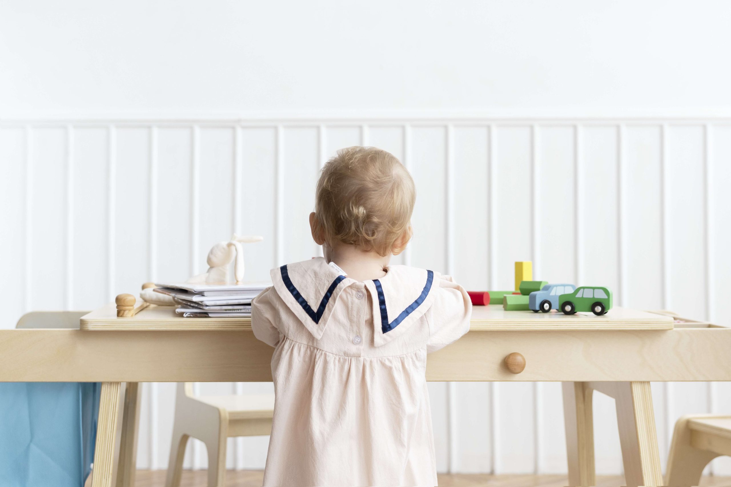 Child with blonde hair playing with toy cars at a wooden desk.
