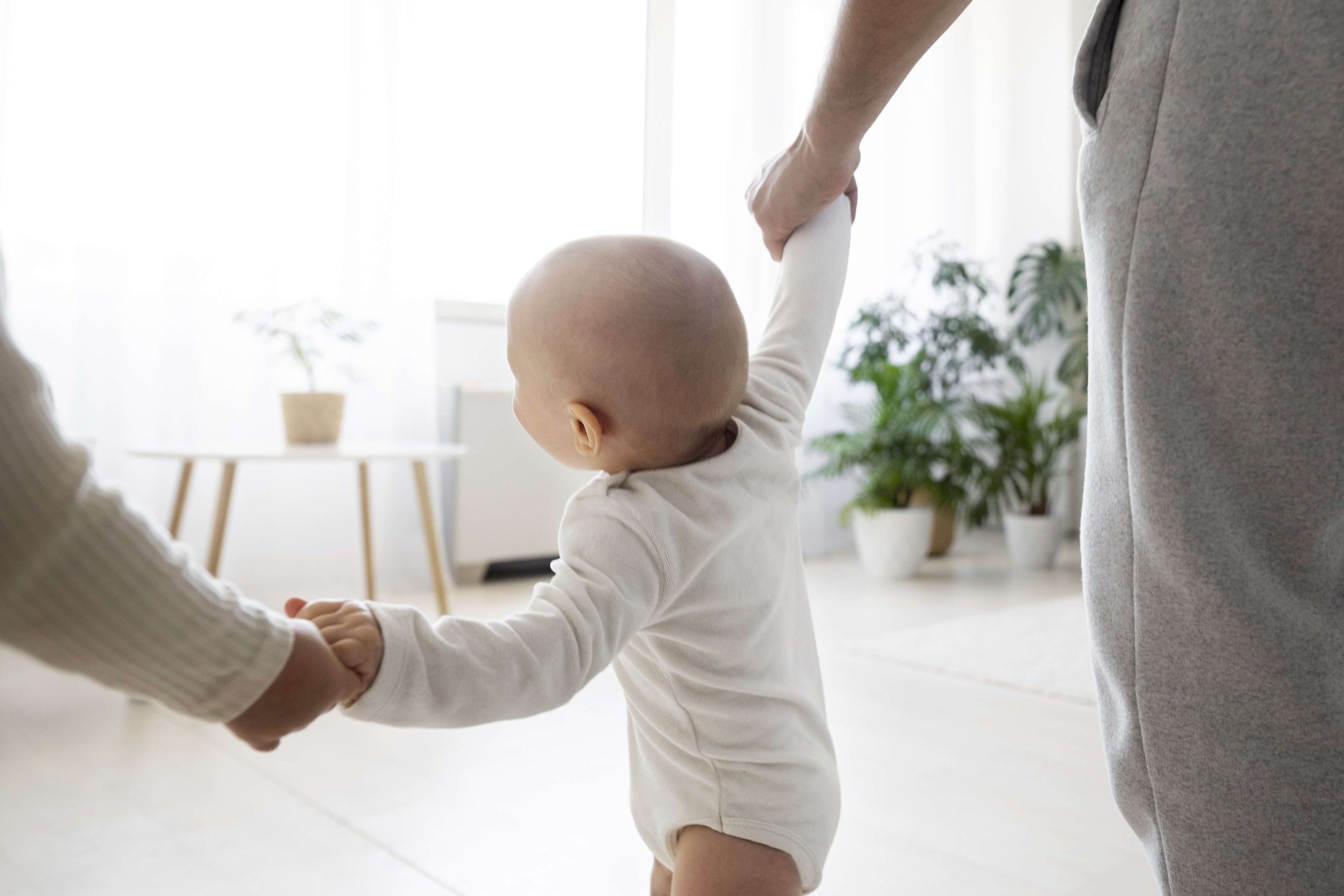 Child with Apert Syndrome holding hands with adults in a bright room.