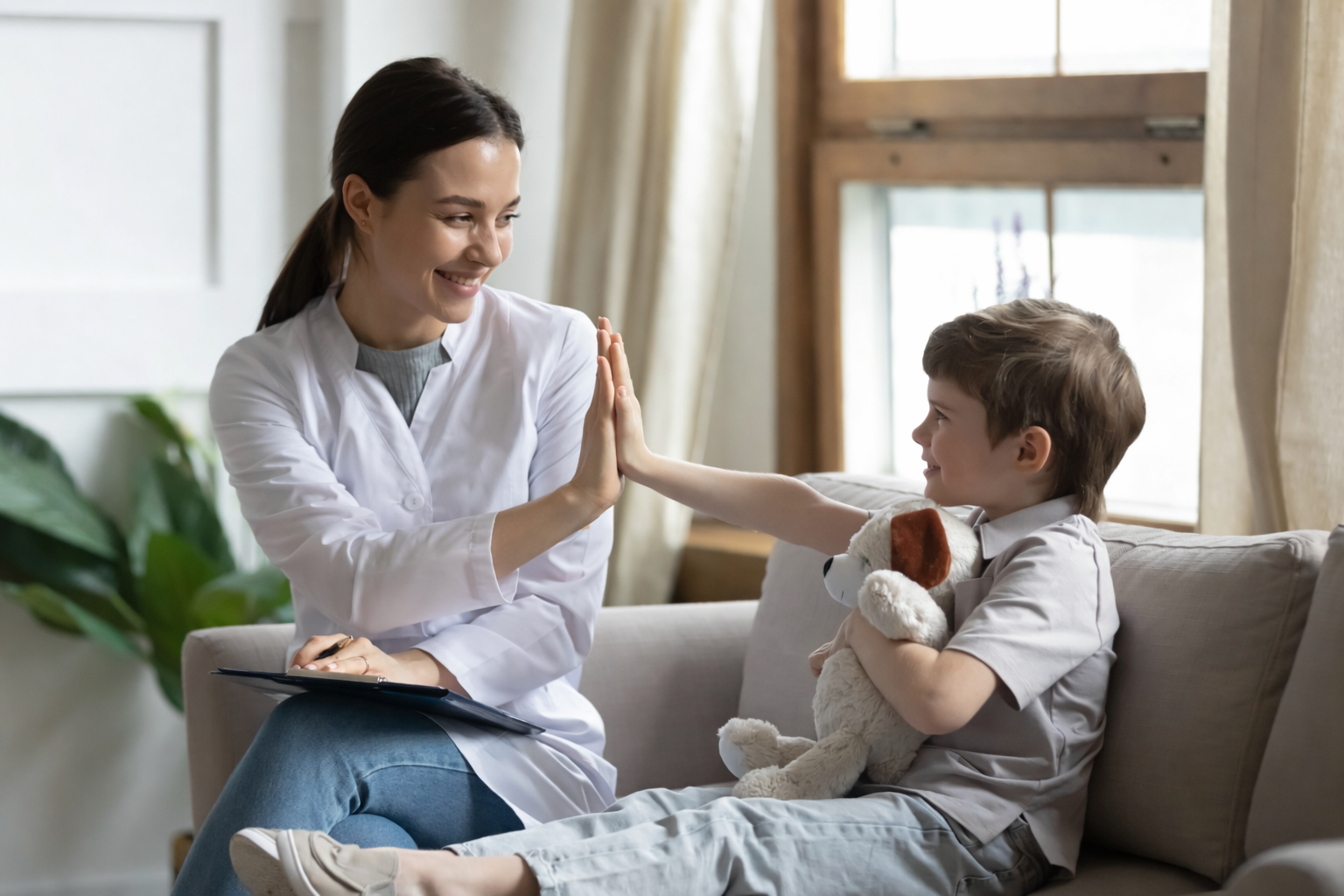 kidwithstufftohappywithdoctor Friendly female doctor playing with child holding teddy bear