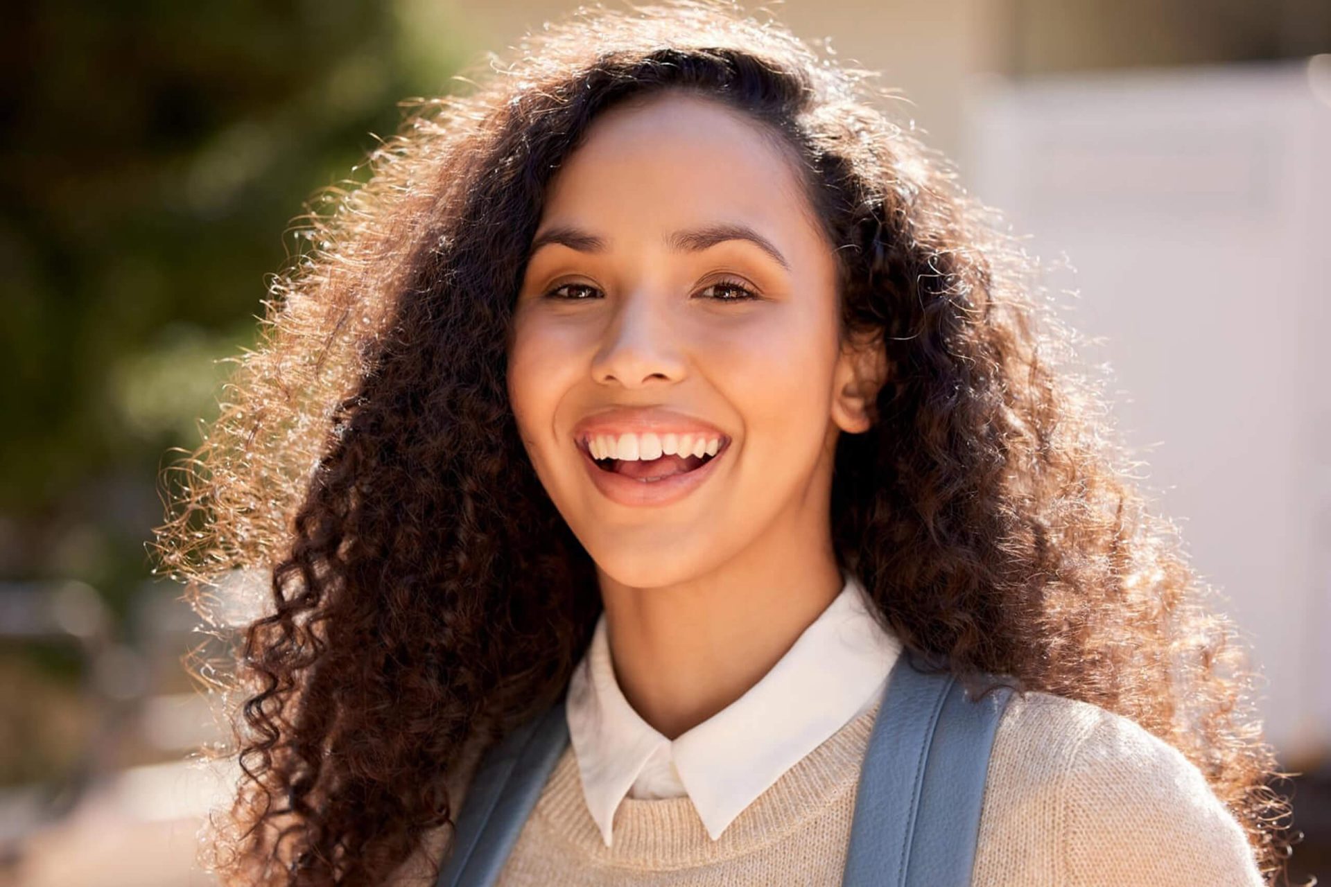 Smiling young woman with curly hair outdoors in sunlight.