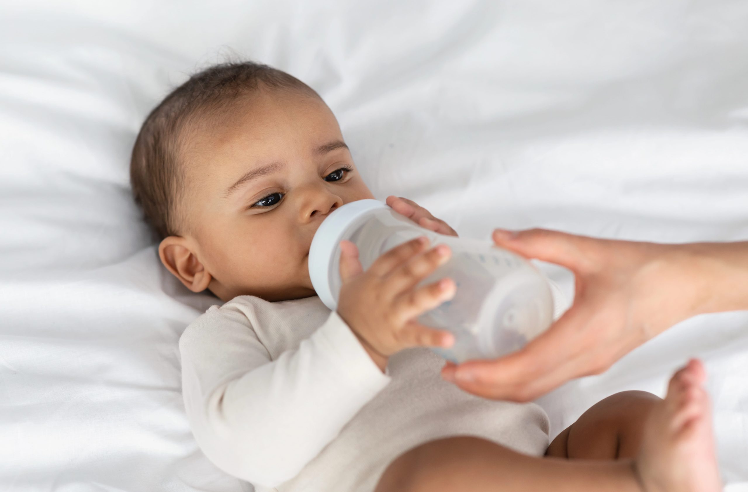 Young child drinking milk from a bottle held by an adult.
