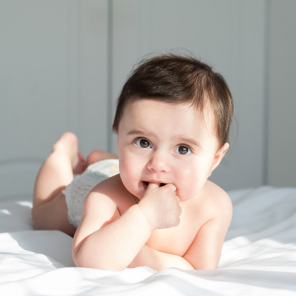 Infant lying on floor with hand in mouth