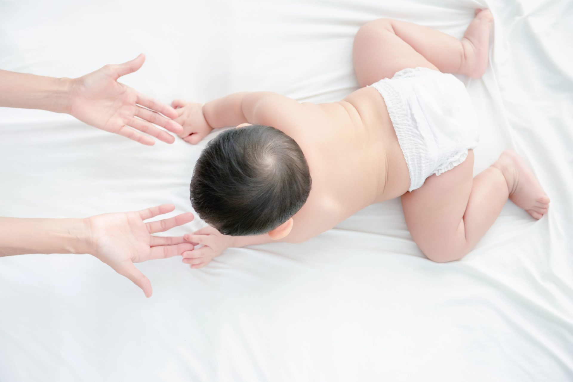 Baby lying on bed with hands reaching towards him, post cleft palate repair.