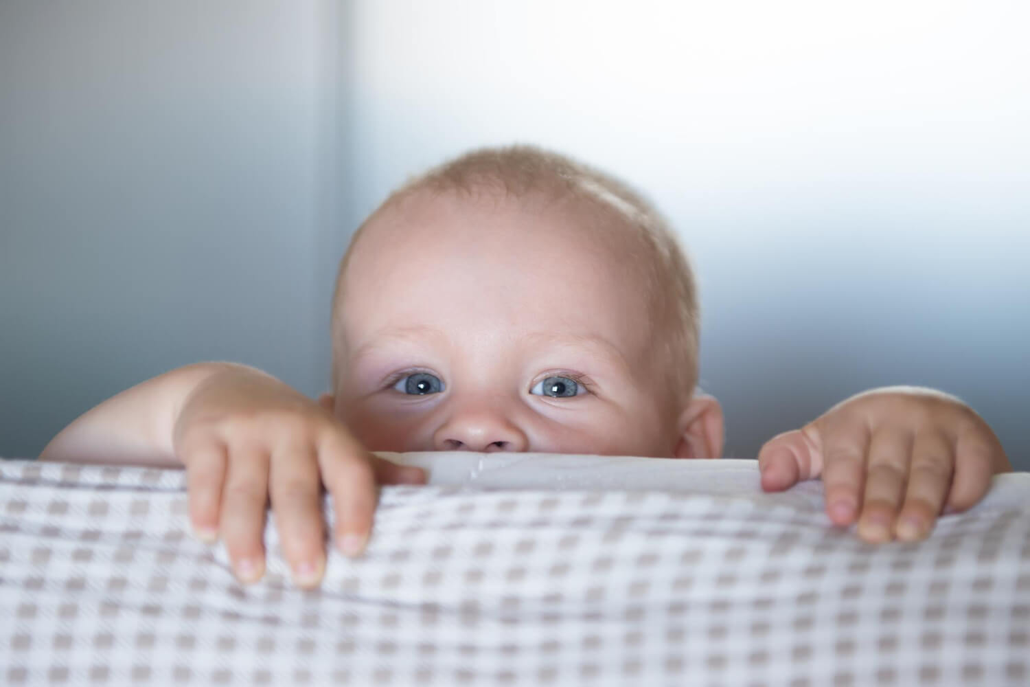Baby peeking over a bed with a visible unilateral cleft lip.