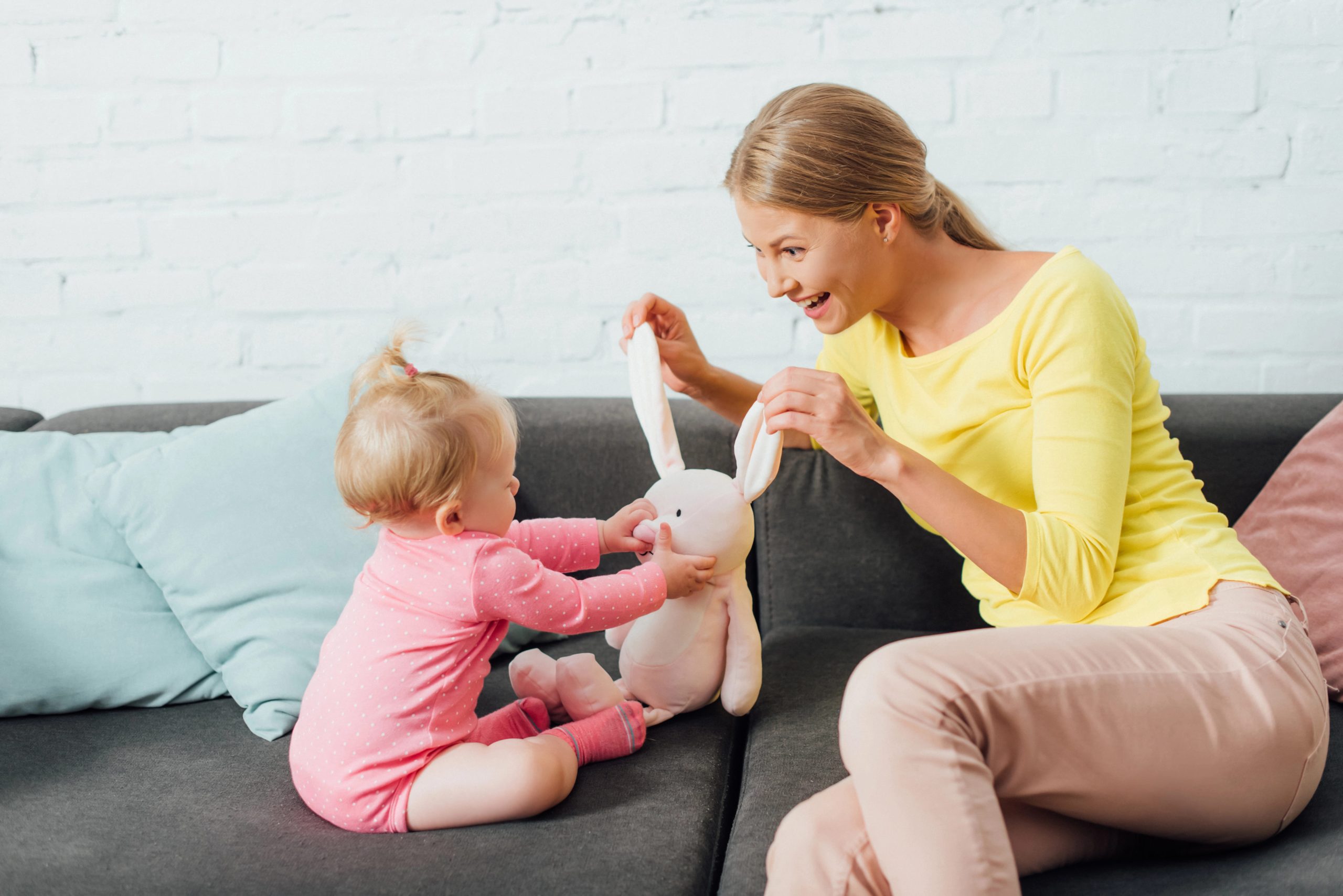 Mother and young girl playing with a stuffed bunny on a sofa.