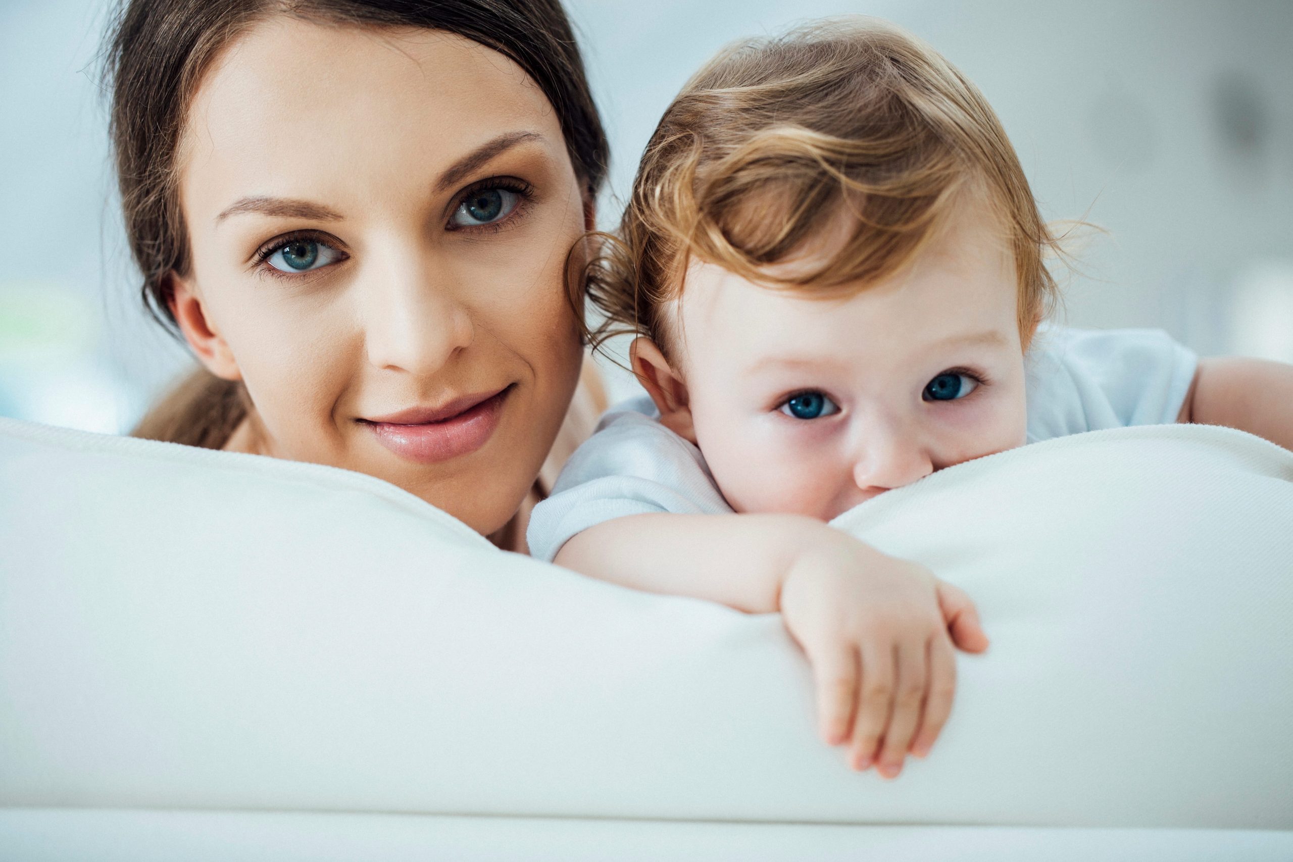 Mother and young child lying on a white surface, looking at the camera.
