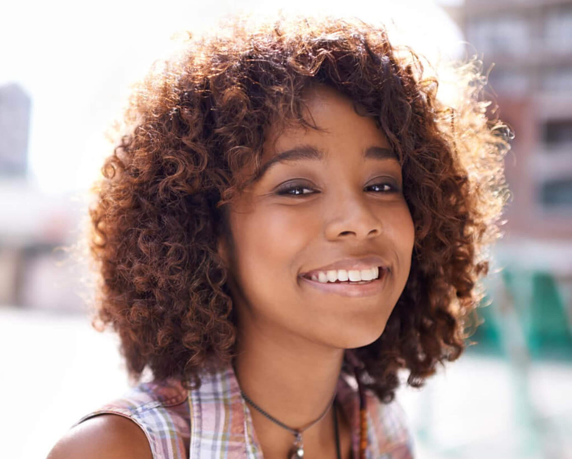 Happy young woman with curly hair smiling outdoors in urban setting.