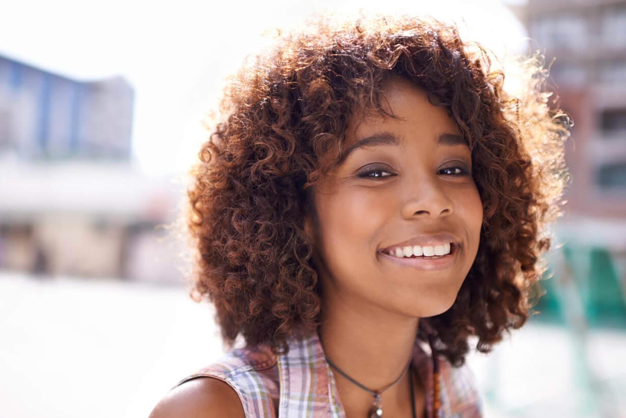 Happy young woman with curly hair smiling outdoors in urban setting.