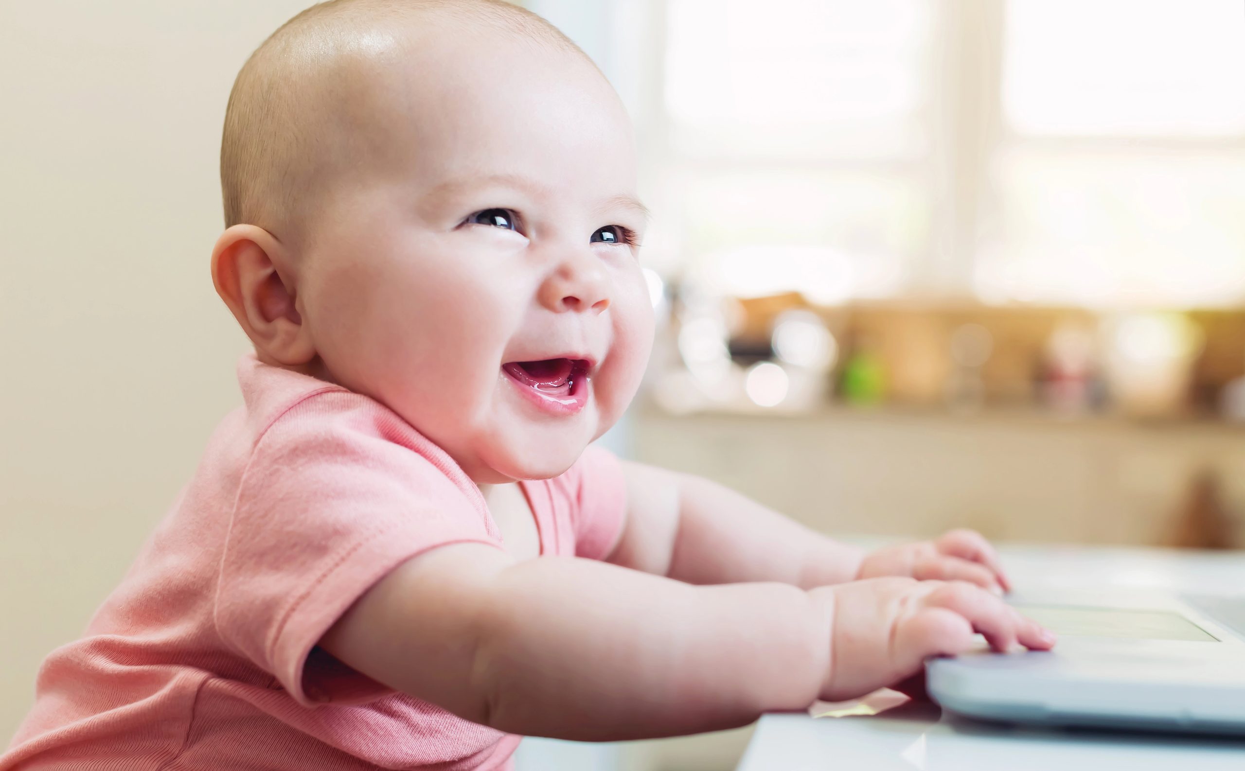 Smiling infant supporting themself on a table, illustrating healthy development during follow-up care.