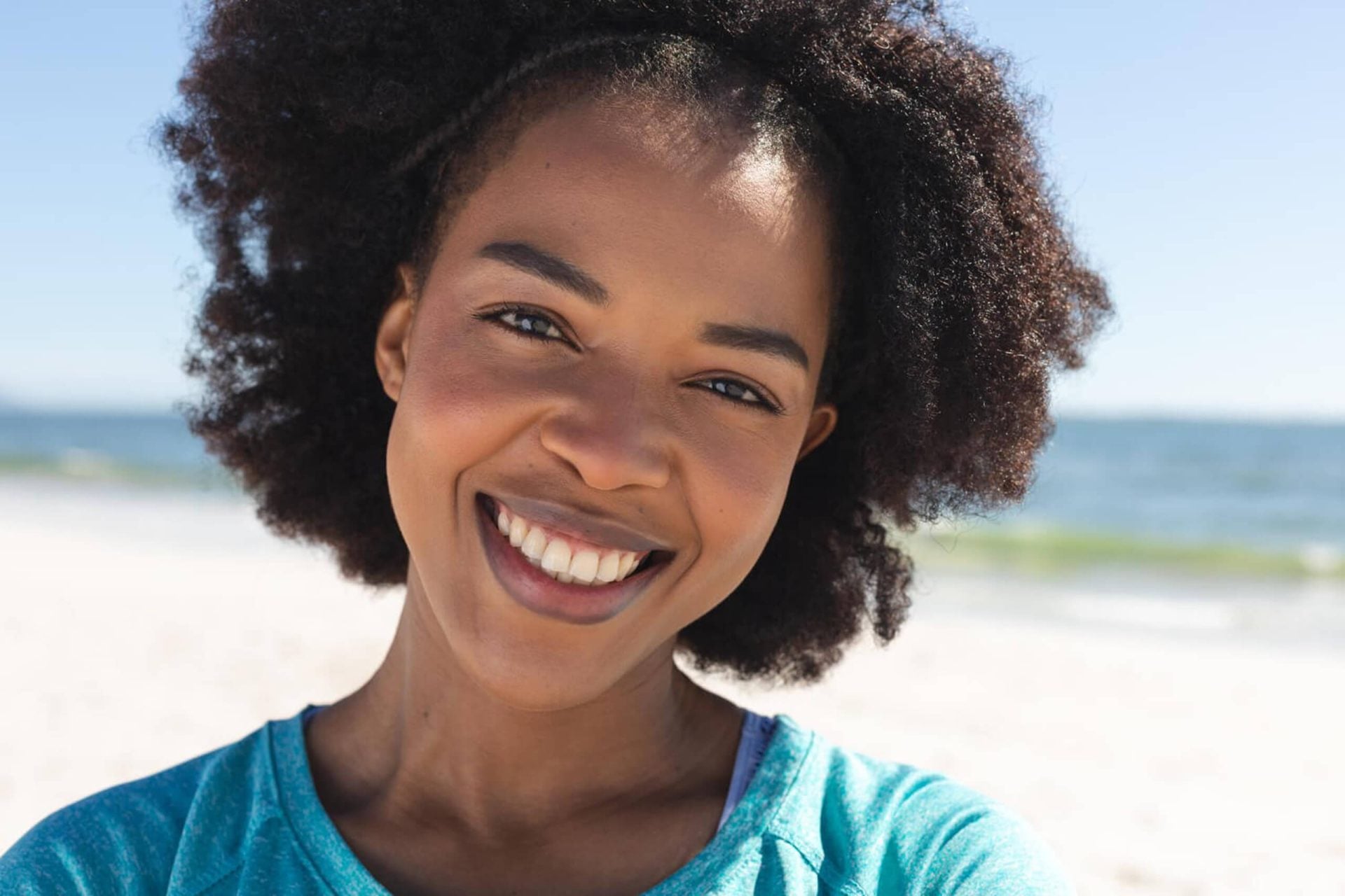 Happy woman smiling at the beach with ocean in background.
