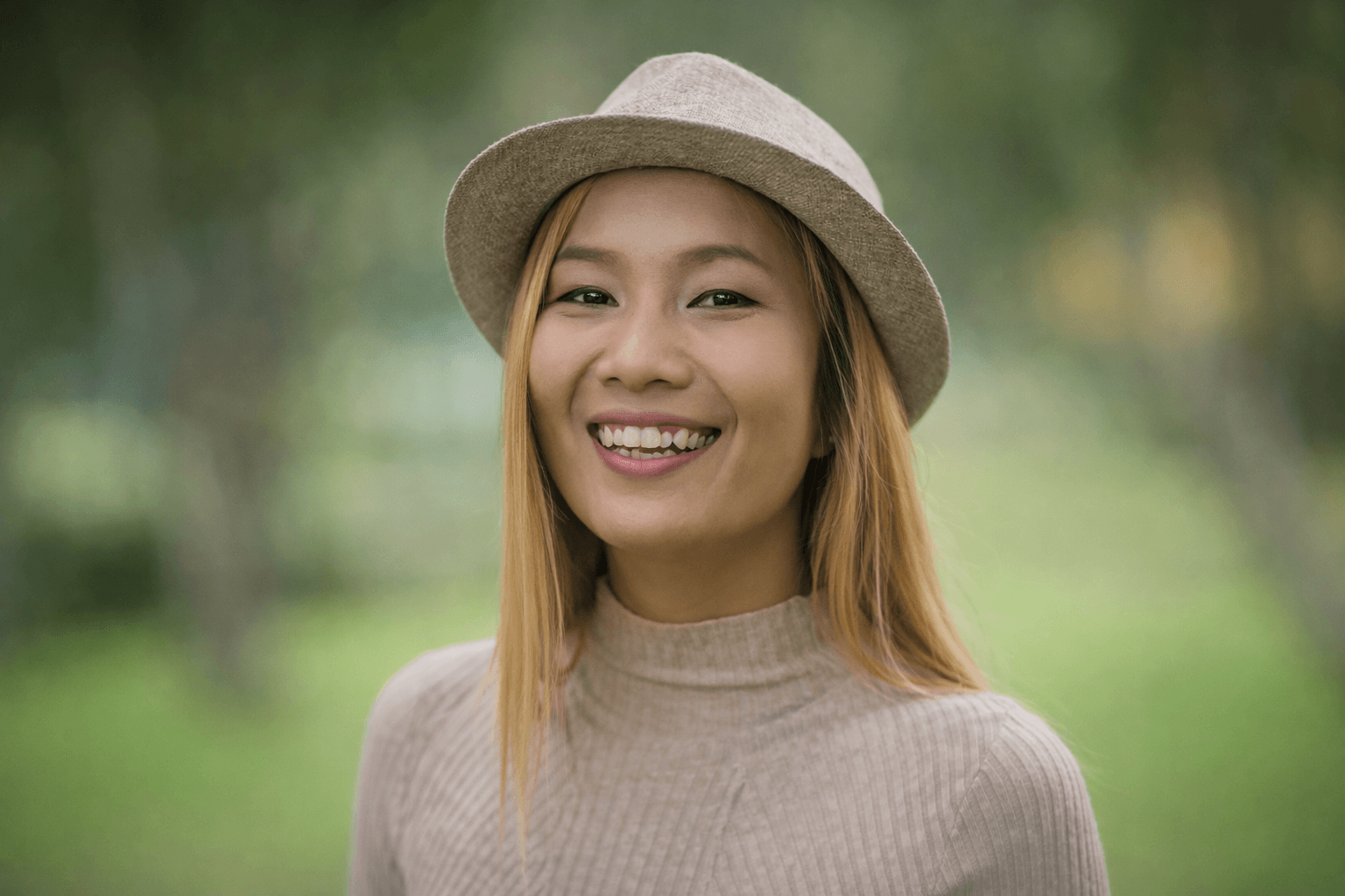 Happy woman with a hat smiling in a natural outdoor setting.