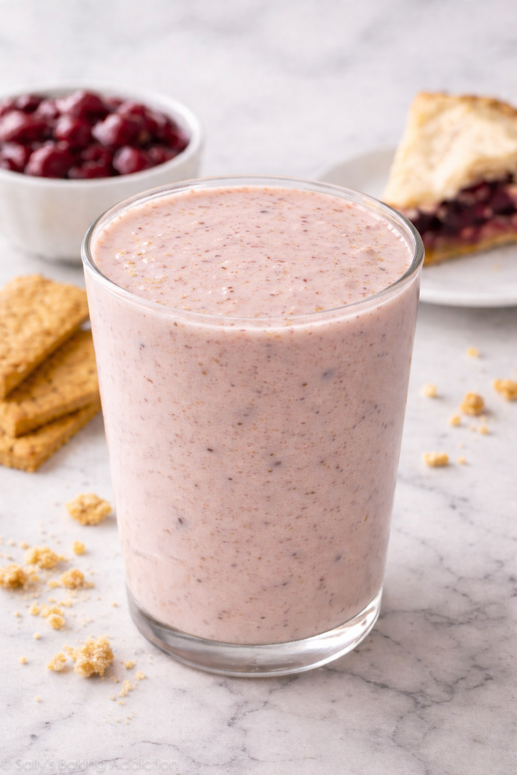 Creamy strawberry milkshake in a glass with a berry pie and cookies in the background.