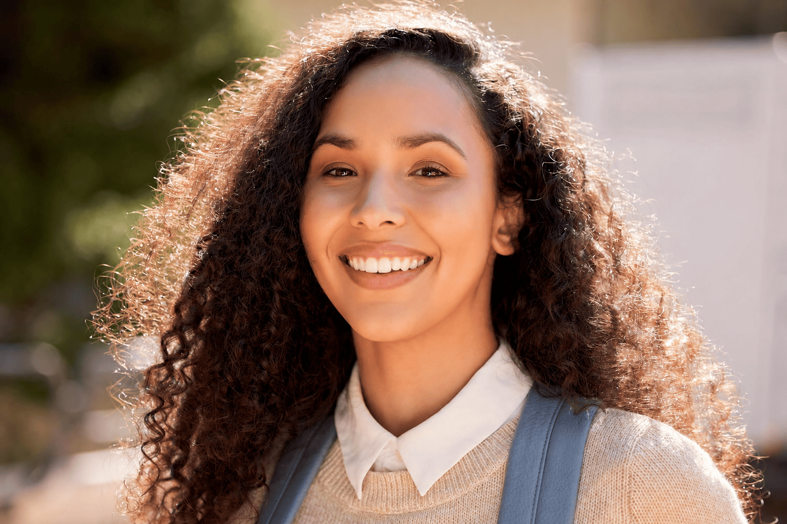 Happy young woman with curly hair smiling in natural sunlight.