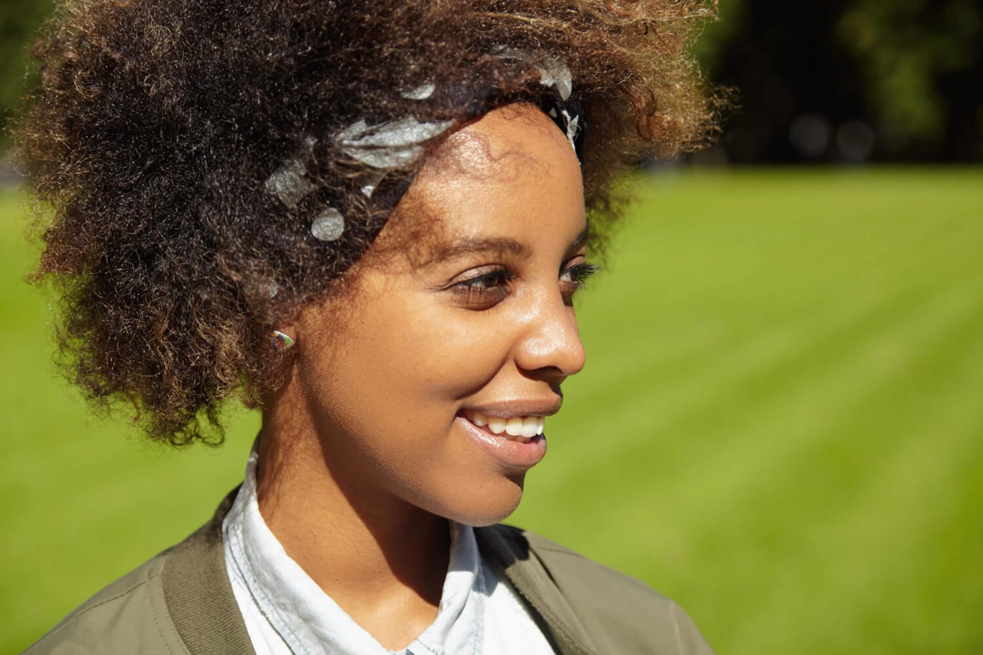 Smiling young woman with natural curly hair outdoors in sunlight.